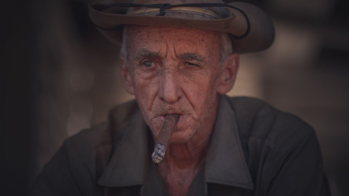Elderly man wearing a cowboy hat with a focused gaze, cigar in hand.
