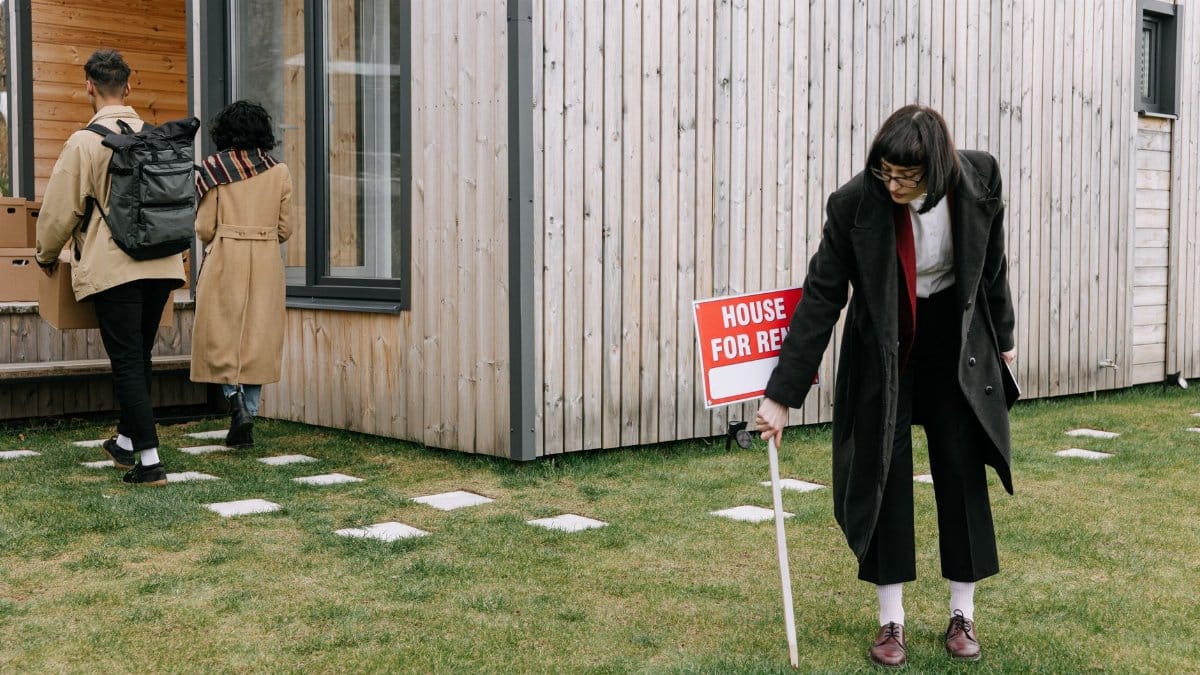 A couple moving into a new rental house as a real estate agent places a sign outside.