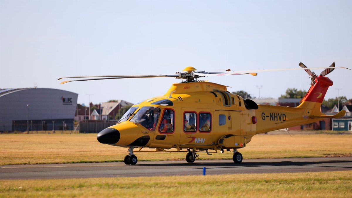 Bright yellow rescue helicopter with visible rotor at airport, ready for takeoff.