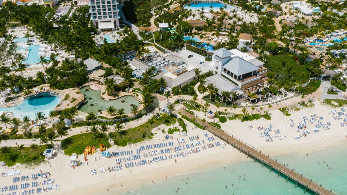 An aerial shot of a vibrant beach resort with clear waters, lush greenery, and modern architecture.