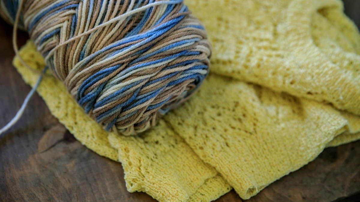 Close-up of a ball of colorful wool yarn next to a knitted yellow sweater.