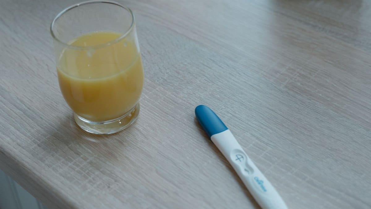 A glass of orange juice and a positive pregnancy test placed on a wooden table.