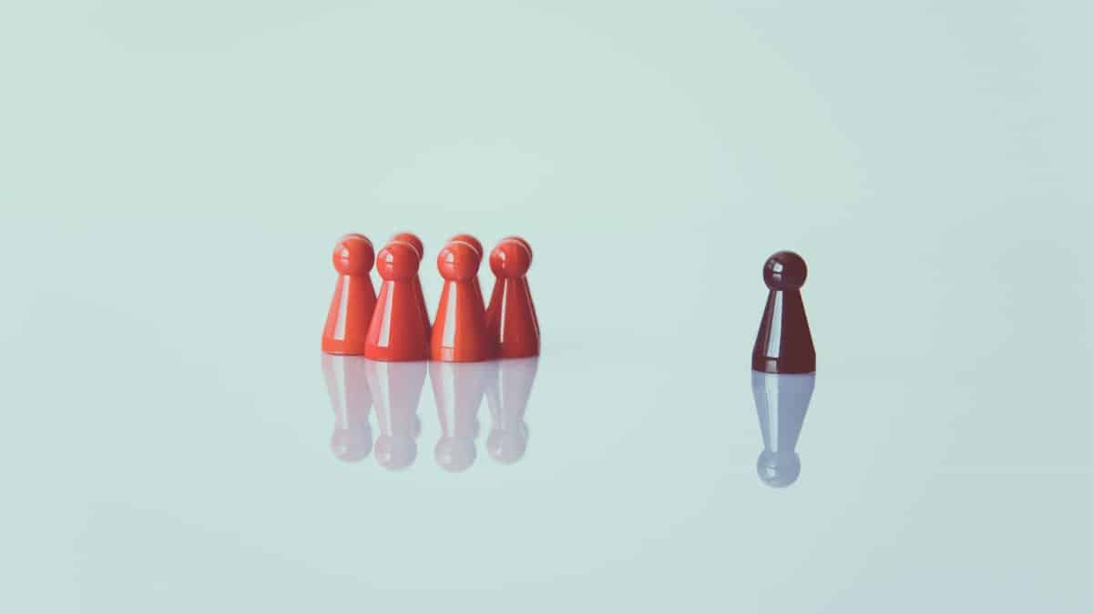 Red game pieces grouped with one isolated piece symbolizing social distancing on a reflective surface.