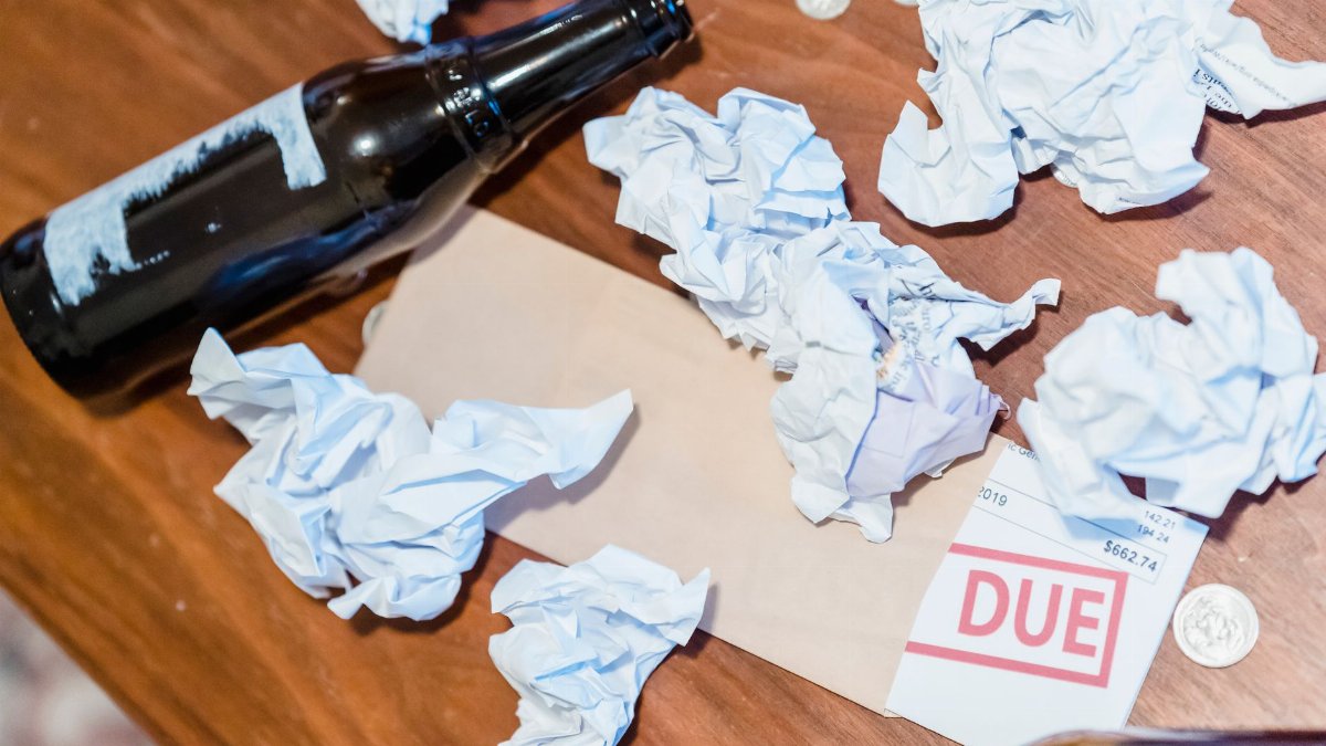 A chaotic scene with overdue bill, beer bottles, and crumpled papers on a wooden table.