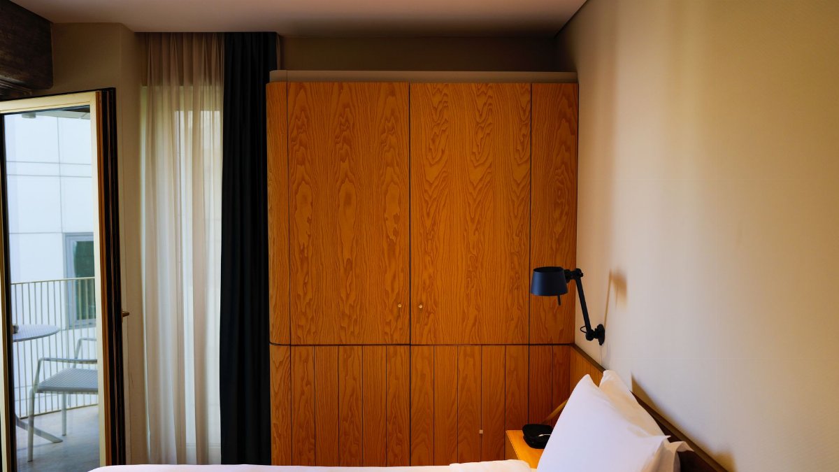 A contemporary hotel room featuring a wooden wardrobe, bed, and balcony access for a comfortable stay.