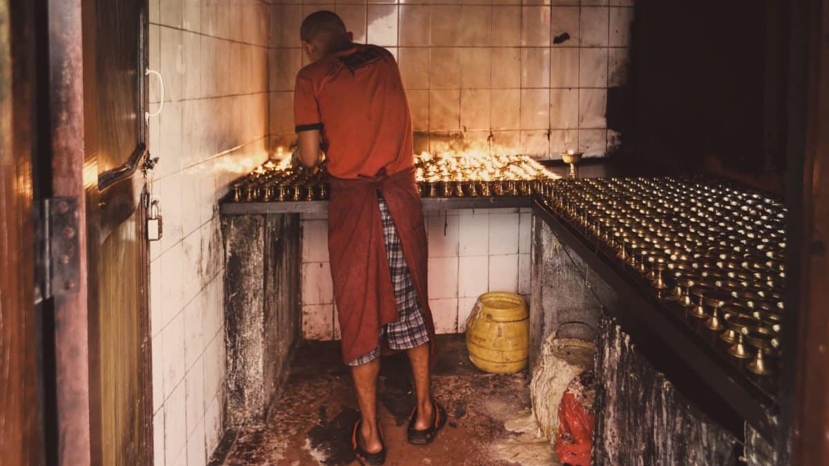A monk lighting numerous candles in a dimly lit room, creating a serene atmosphere.