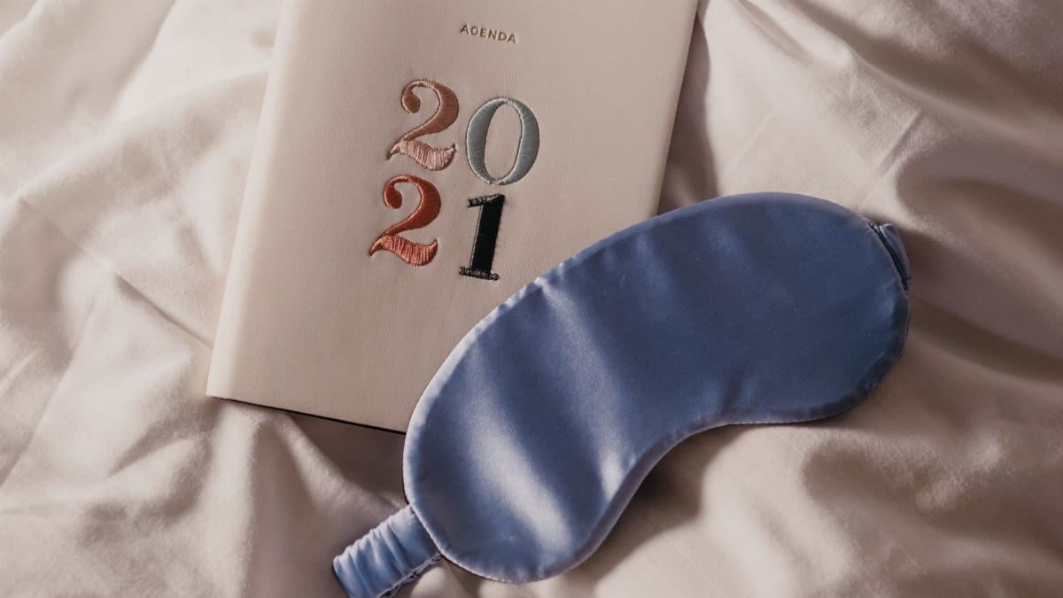 Cozy setup of 2021 agenda and eye mask on satin sheets, perfect for relaxation.