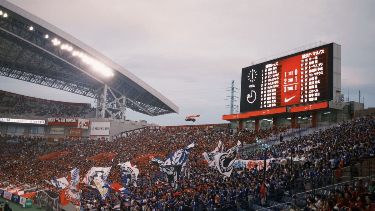 A lively soccer stadium scene with fans waving flags and a scoreboard displaying match details.