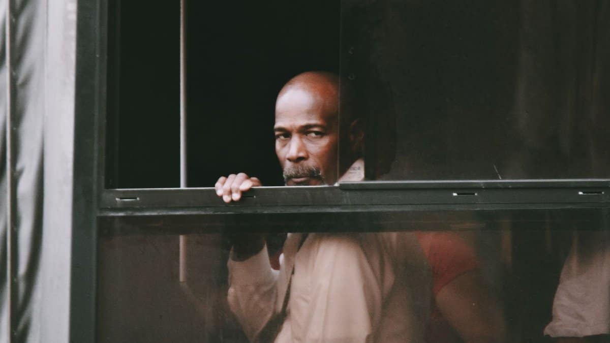 Bald man reflects while looking out of a window with a thoughtful expression.