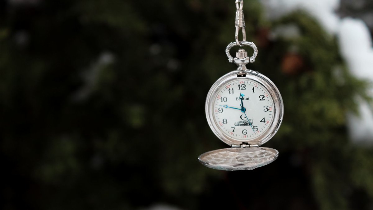 Close-up of a silver pocket watch hanging with blurred natural background.