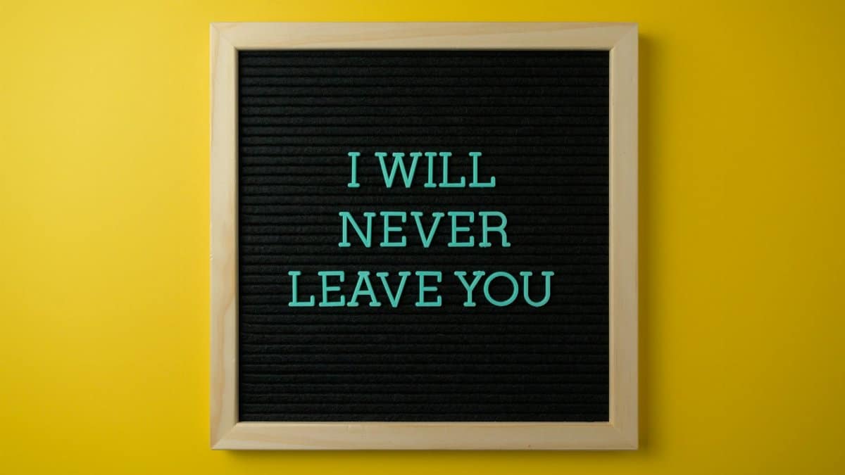 Inspirational quote 'I Will Never Leave You' on a black letter board against a yellow wall.