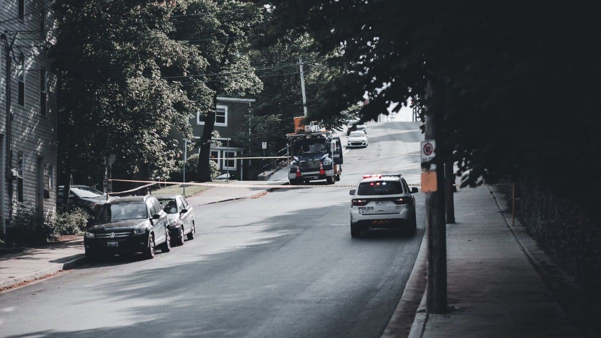 Police vehicle driving on a tranquil city street, surrounded by trees and parked cars.