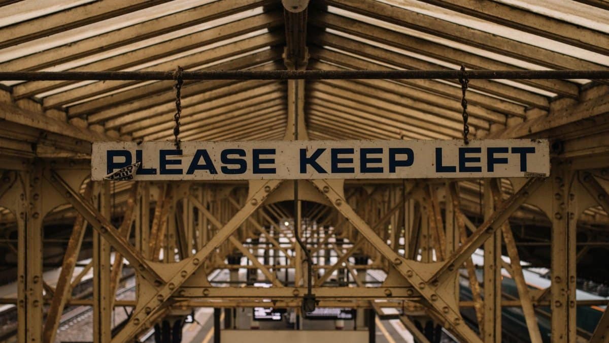 Vintage metal construction on railway station with platform under old roof and sign saying Please keep left