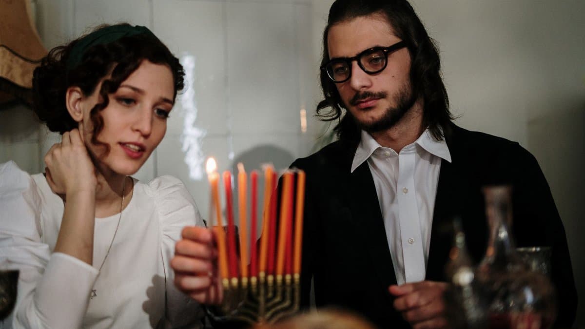 An intimate moment of a couple lighting a menorah during Hanukkah celebration at home.