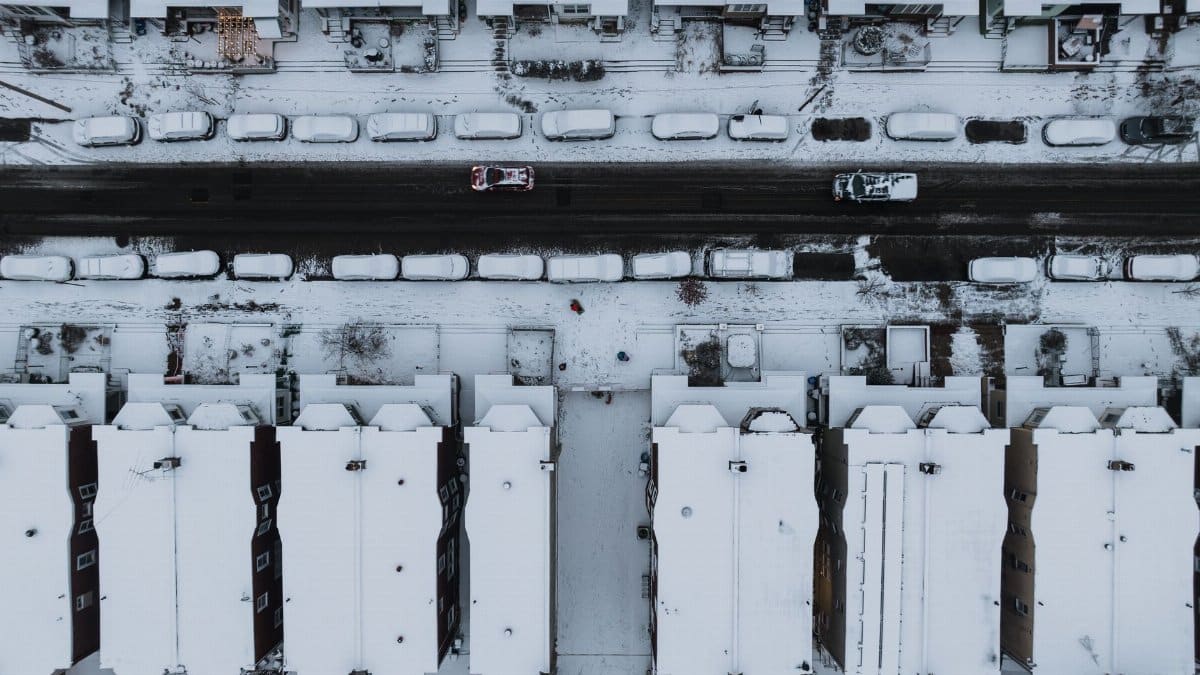 Aerial view of snow-covered street in Philadelphia, showcasing rooftops and parked cars.