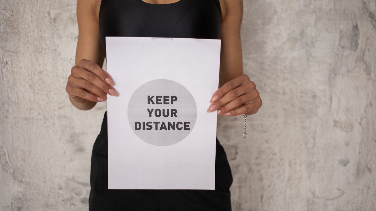 Crop unrecognizable African American female athlete in sportswear standing with poster saying keep your distance against gray concrete wall
