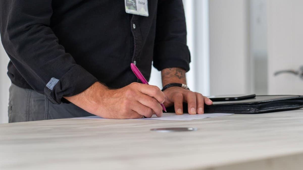 A businessman signing documents at a modern office desk with a focus on hands and workspace.