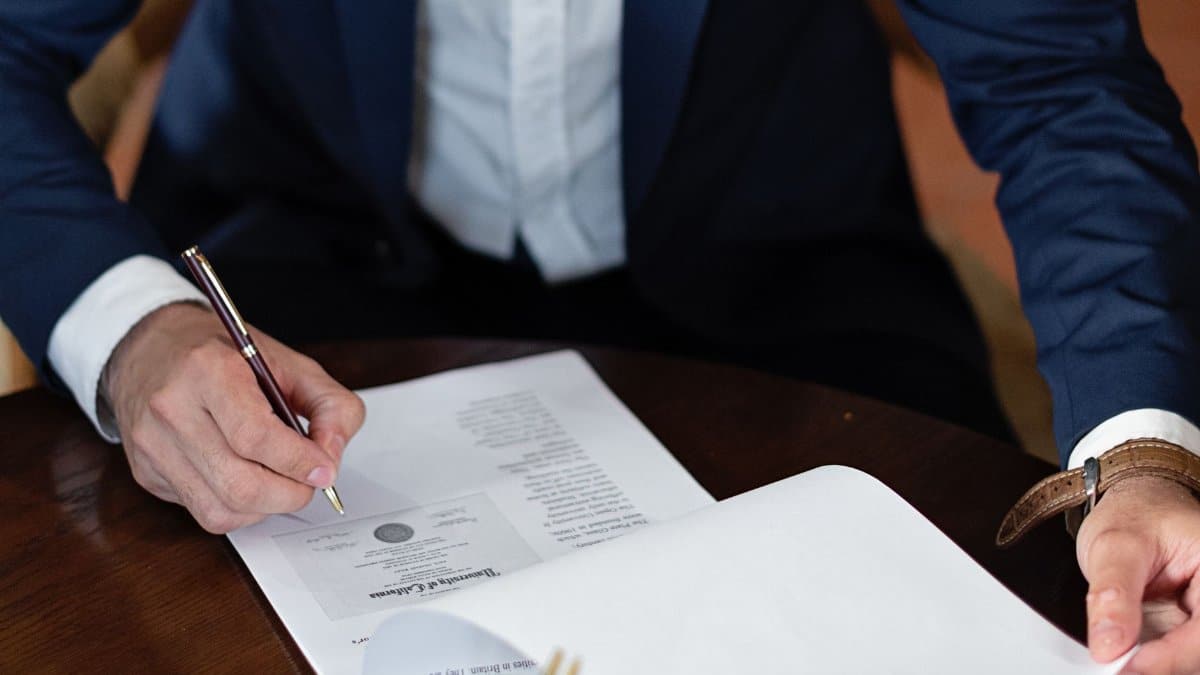 A professional individual signs legal documents at a desk in an office setting.