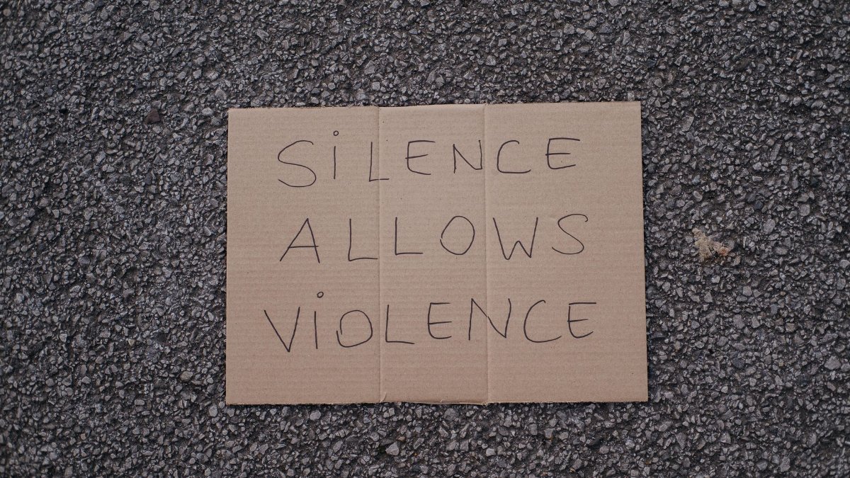 Top view of slogan silence allows violence on carton placed on rough asphalt road on street