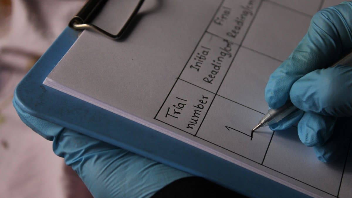 Close-up of a gloved hand writing in a lab notebook, documenting trial readings.