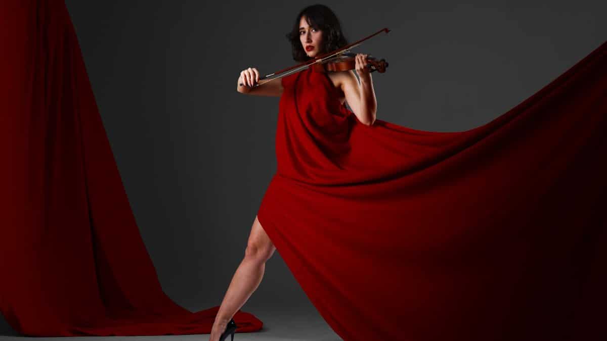 Violinist in a flowing red dress playing indoors, exuding elegance and poise.