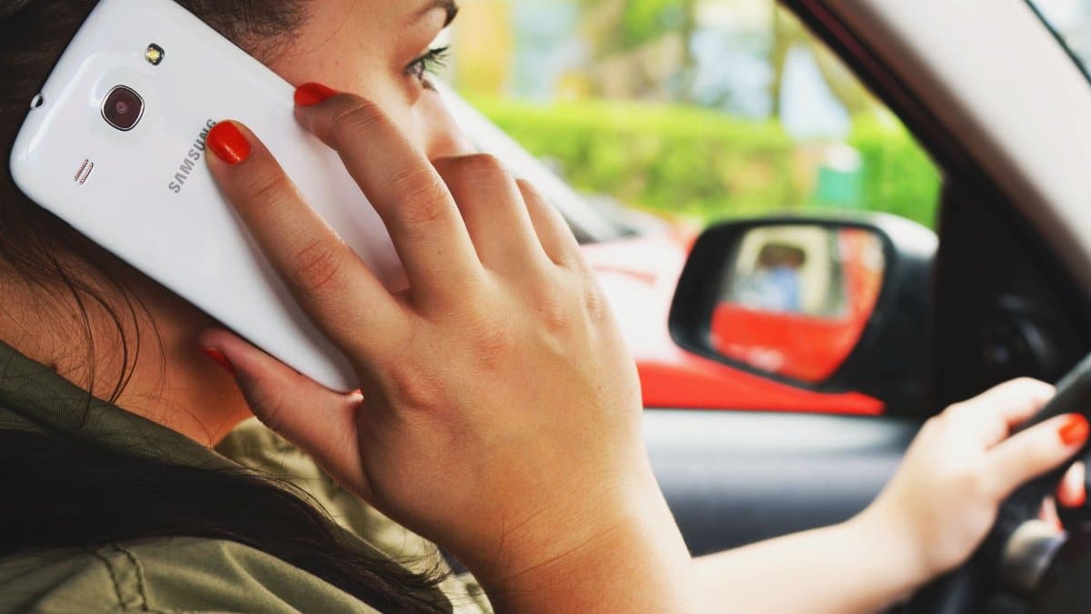 Close-up of a woman driving a car while talking on a smartphone, highlighting road safety concerns.