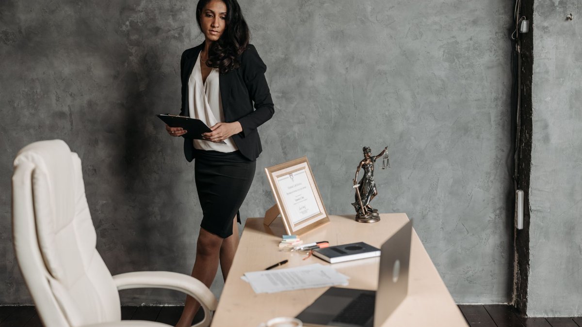 Confident businesswoman in a formal setting with legal papers and a statue of justice on the desk.