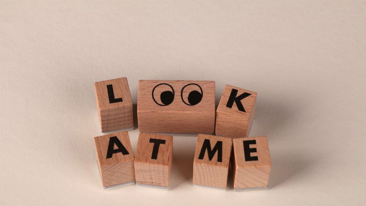 Playful wooden blocks display the phrase 'Look At Me' on a neutral background, featuring cartoon eyes.