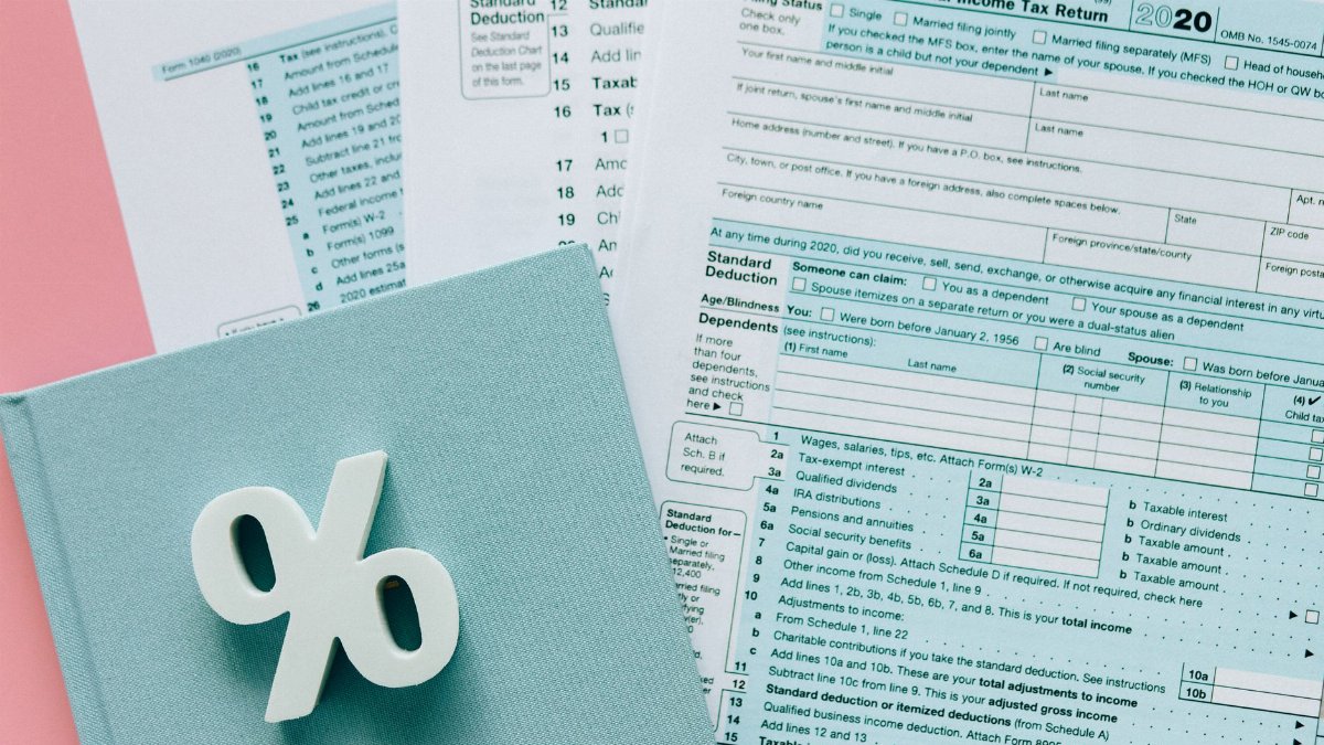 Tax documents with a percentage symbol on a pink and blue desk setup, emphasizing finance.