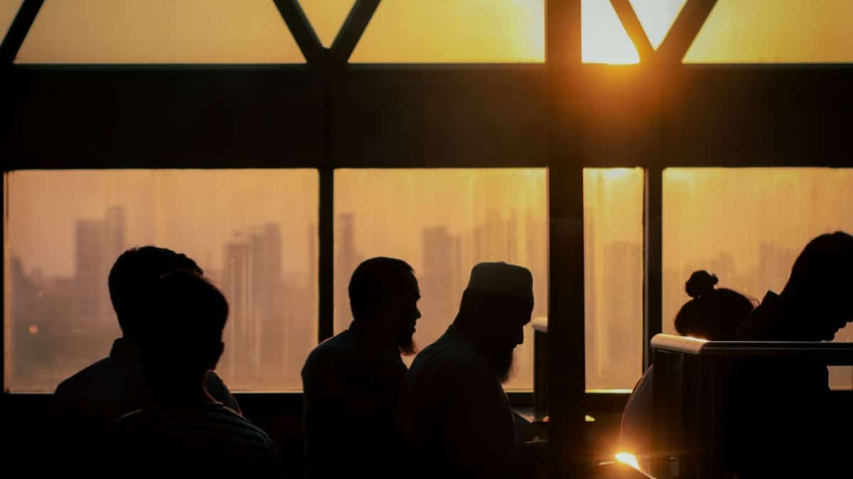 Silhouettes of people inside a building at sunset, overlooking a distant city skyline through a window.