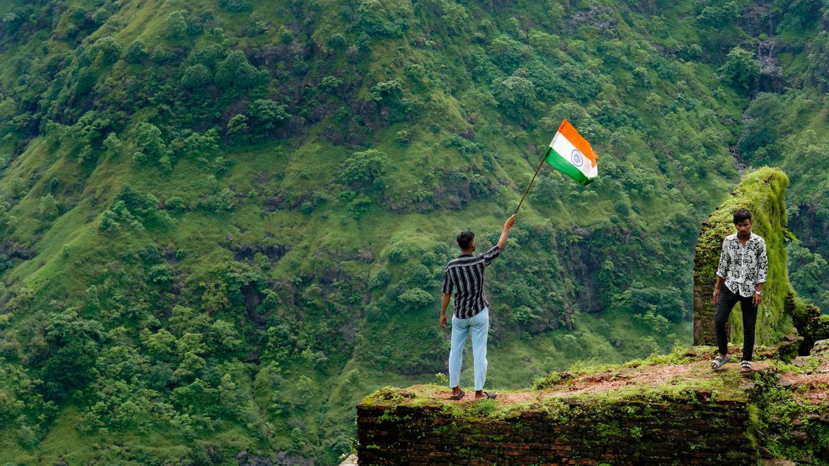 Two men celebrate in vibrant landscape with Indian flag on lush hillside.