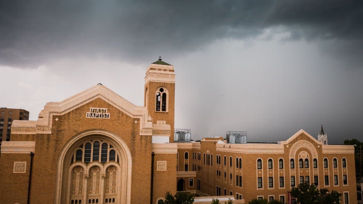 A dramatic view of the First Baptist Church building with ominous storm clouds overhead.