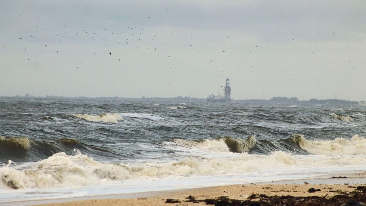 Waves crash onto a sandy beach in Ciudad del Carmen, Mexico, with an offshore rig in view.