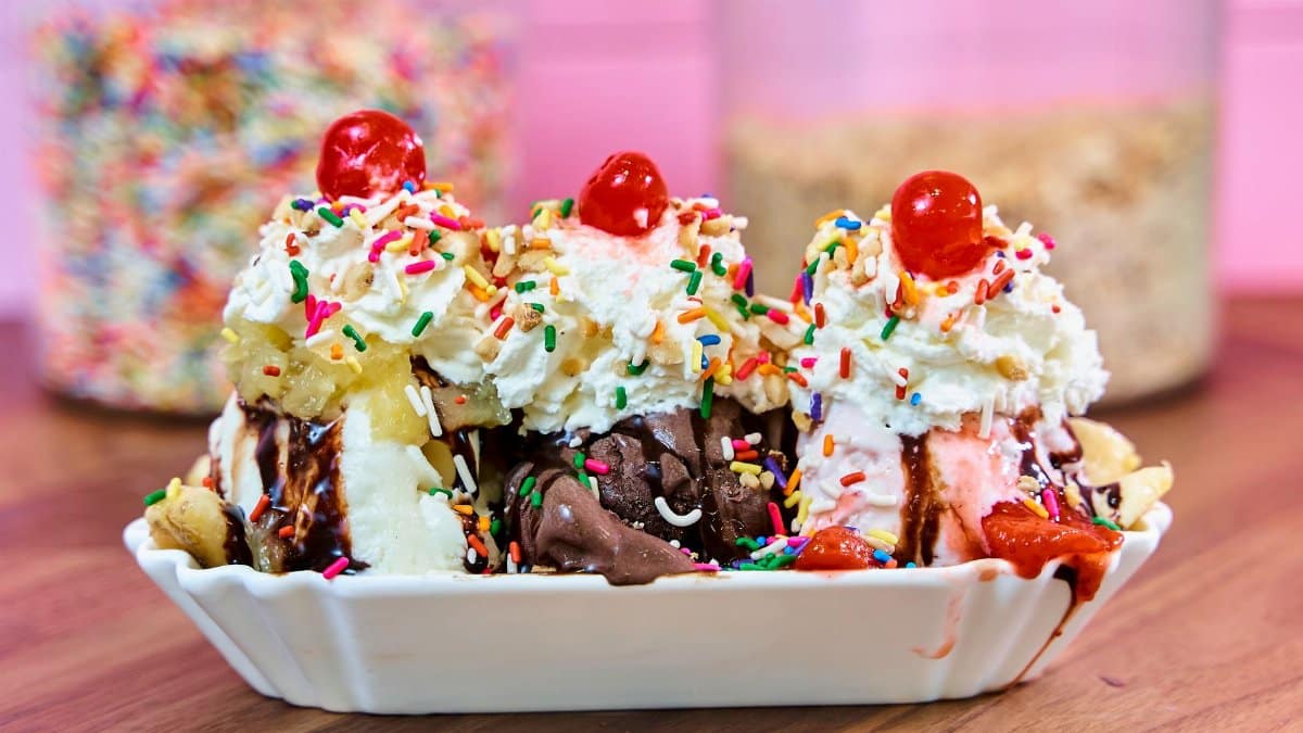 Colorful banana split ice cream sundae topped with whipped cream, cherries, and sprinkles.