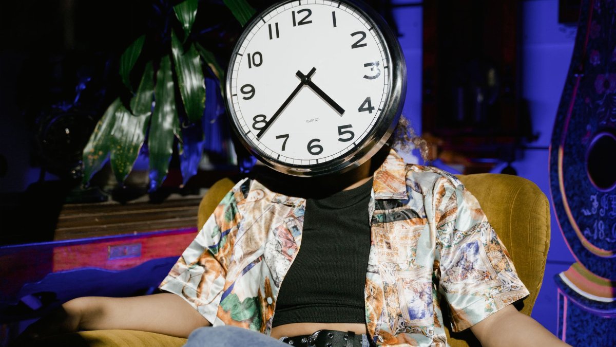 A surreal image of a person sitting in an armchair with a clock as a face, evoking themes of time and identity.