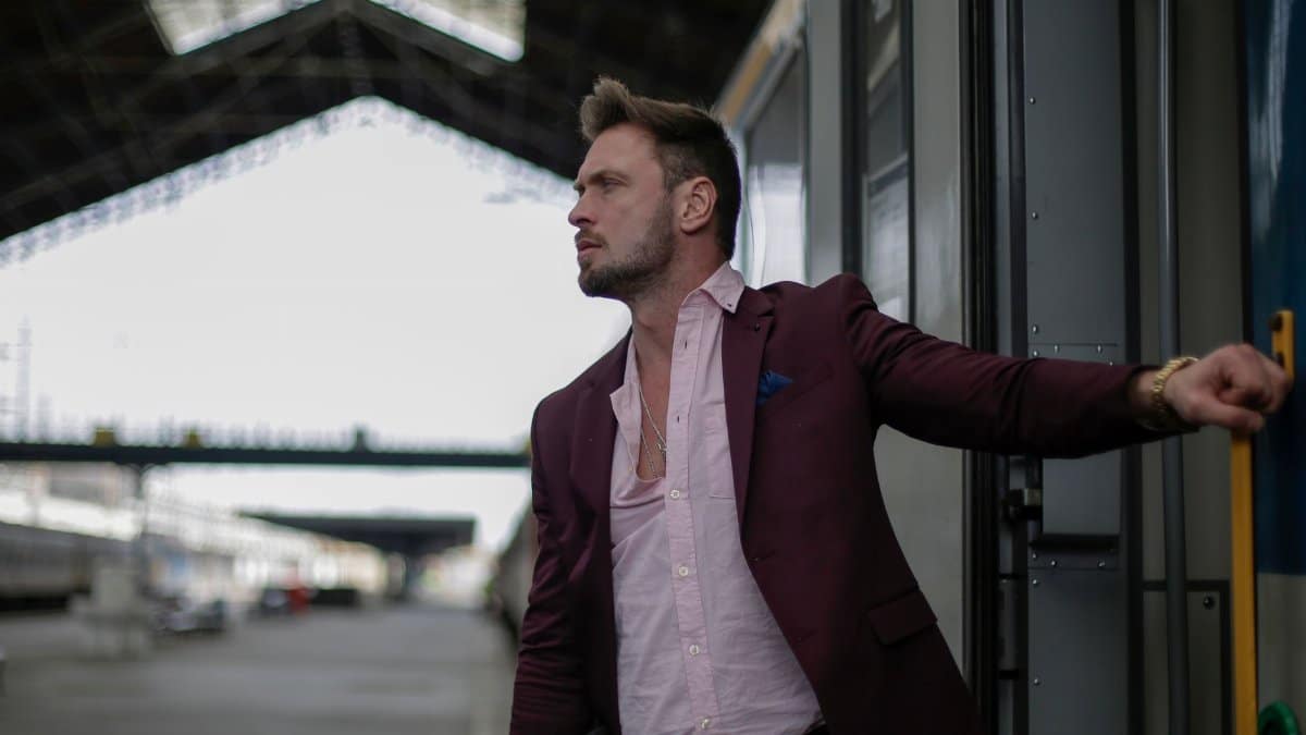 Serious male passenger wearing formal suit leaving train wagon while taking handrail on railroad station during business trip and looking away attentively