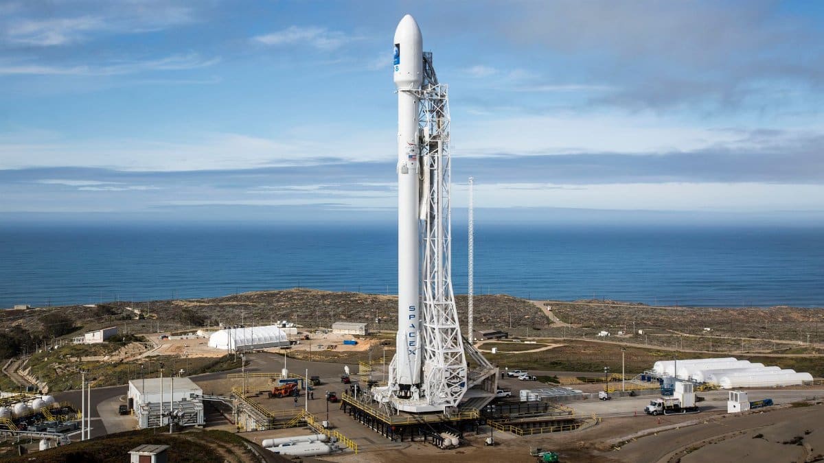 A SpaceX rocket stands on a launch pad overlooking the ocean under a clear sky.
