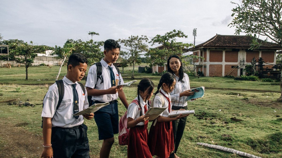 Group of students in school uniforms reading outdoors with their teacher on a sunny day.