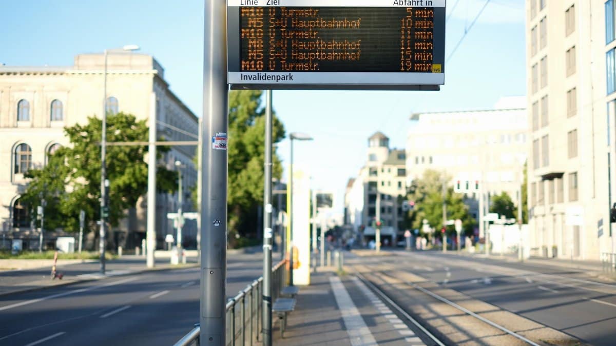 Electronic timetable at a Berlin tram stop with modern urban architecture in the background.