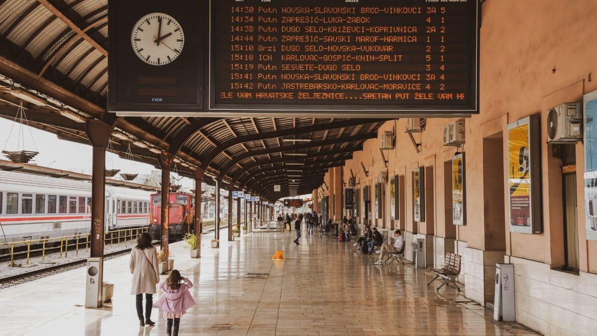 Busy train station in Zagreb with passengers and a large timetable display.