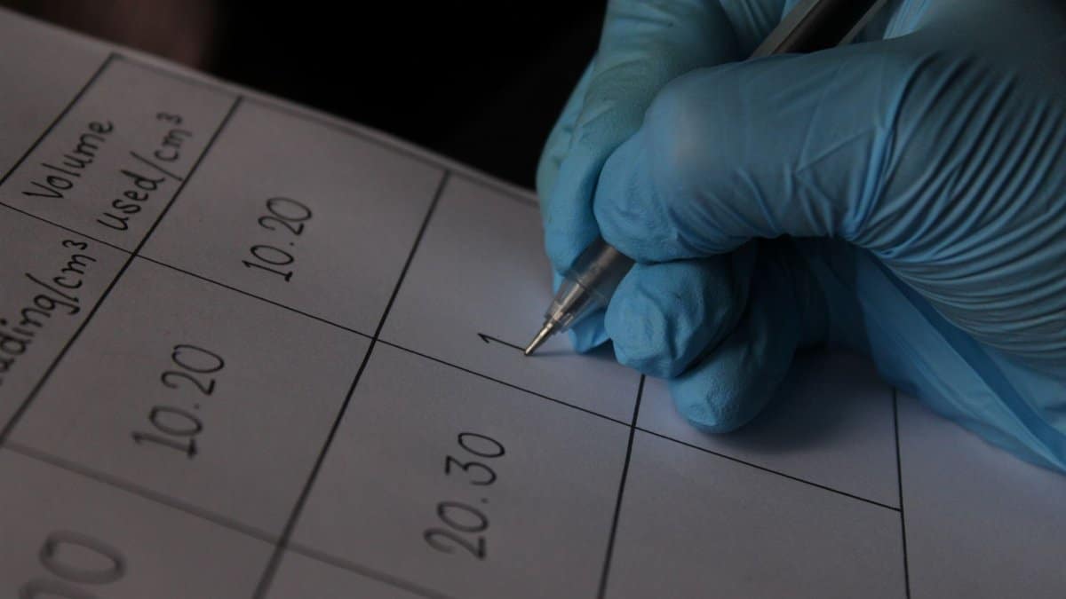 Close-up of a scientist wearing blue gloves writing measurements on a data sheet.