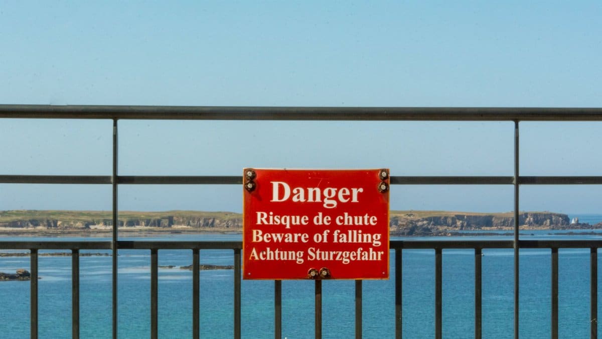 A warning sign on a fence by the sea cautions about falling risks.
