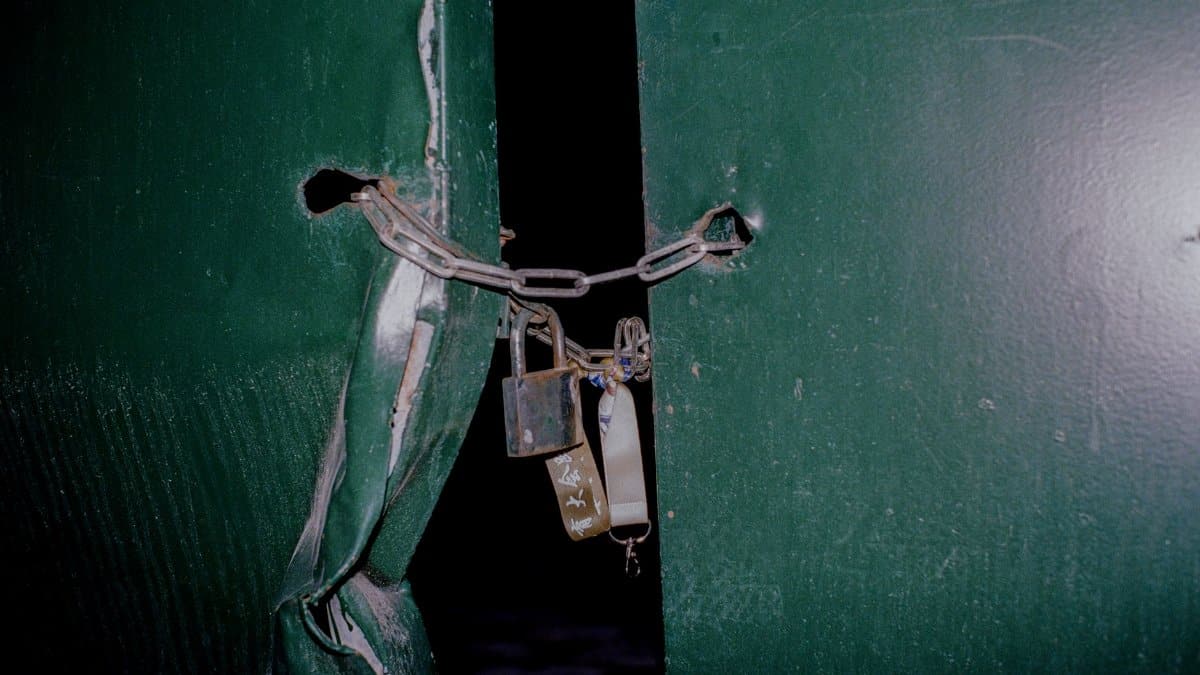 Close-up of a rusty padlock and chain securing green metal doors, blocking entry.