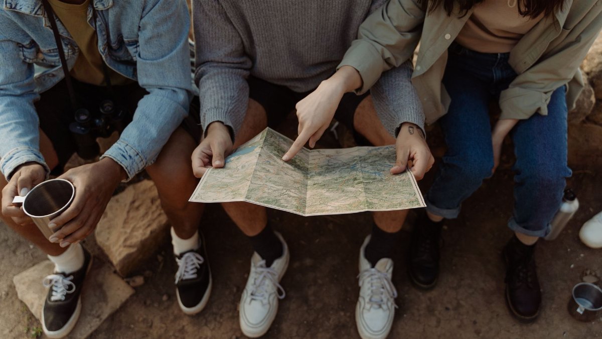Group of friends sitting together, exploring a map for their next adventure, creating exciting travel plans.