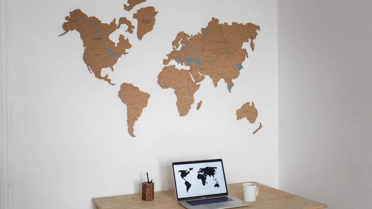 A minimalist workspace with a laptop and cork world map wall art.