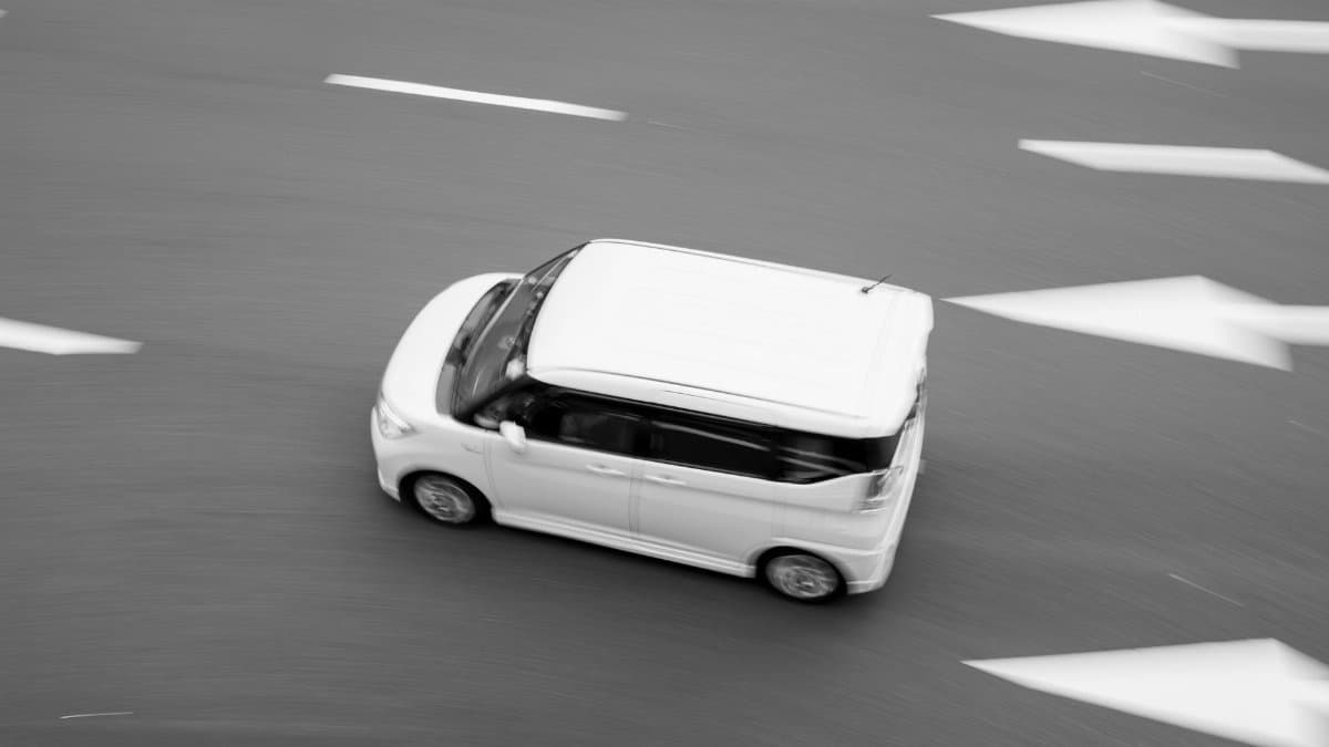 Black and white photo of a moving car on a road with directional arrows, emphasizing motion.