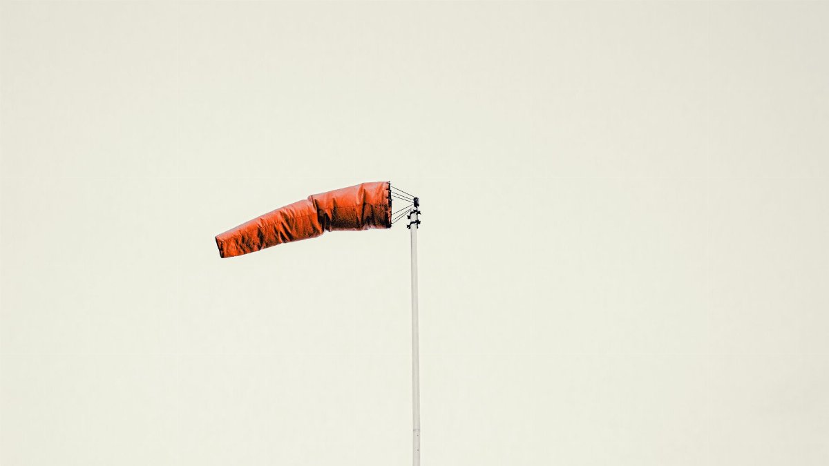 Pole mounted red cone wind sleeve waving against overcast gray sky in daylight