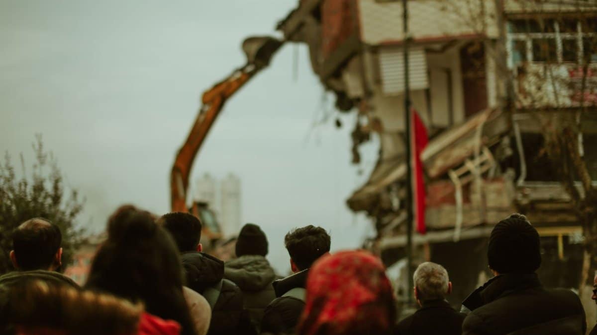 A crowd observes a building being demolished in a cold urban setting.