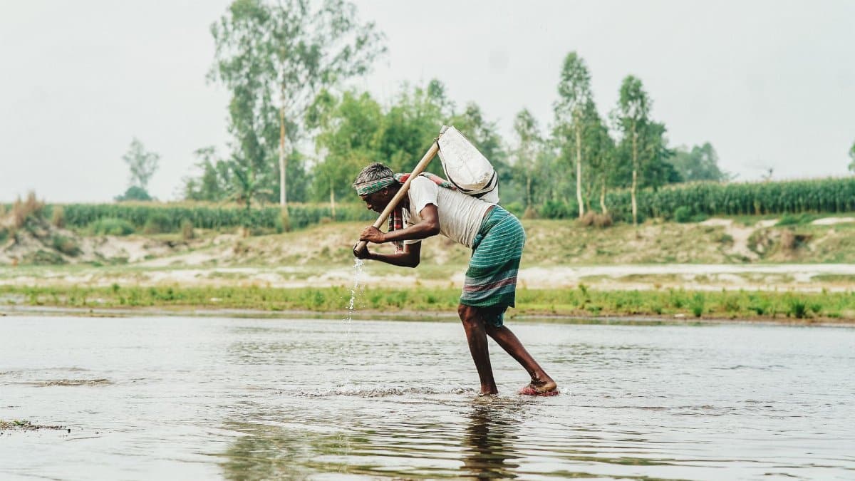 A rural farmer working in a river in a lush green landscape, exemplifying traditional agriculture.