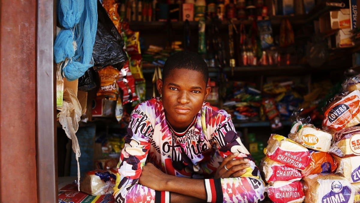 Portrait of a young man in a colorful shirt leaning on a market counter in Abuja, Nigeria.